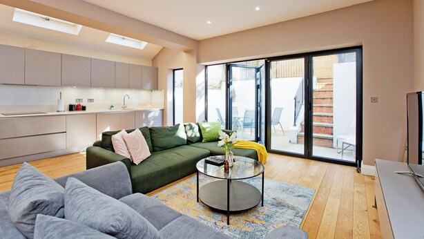 A modern living room with a green sofa, grey couch, and a glass coffee table. - Prime Central Base! 3BR/3BA Apt w/ Courtyard. Ideal for Families and Groups. (London)