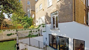 A modern apartment with a balcony, a small garden, and a view of neighboring buildings. - Prime Central Base! 3BR/3BA Apt w/ Courtyard. Ideal for Families and Groups. (London)