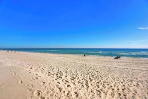 A wide sandy beach with footprints, a clear blue sky, and calm ocean waves. - Crystal Shores 905 by Liquid Life (Gulf Shores)