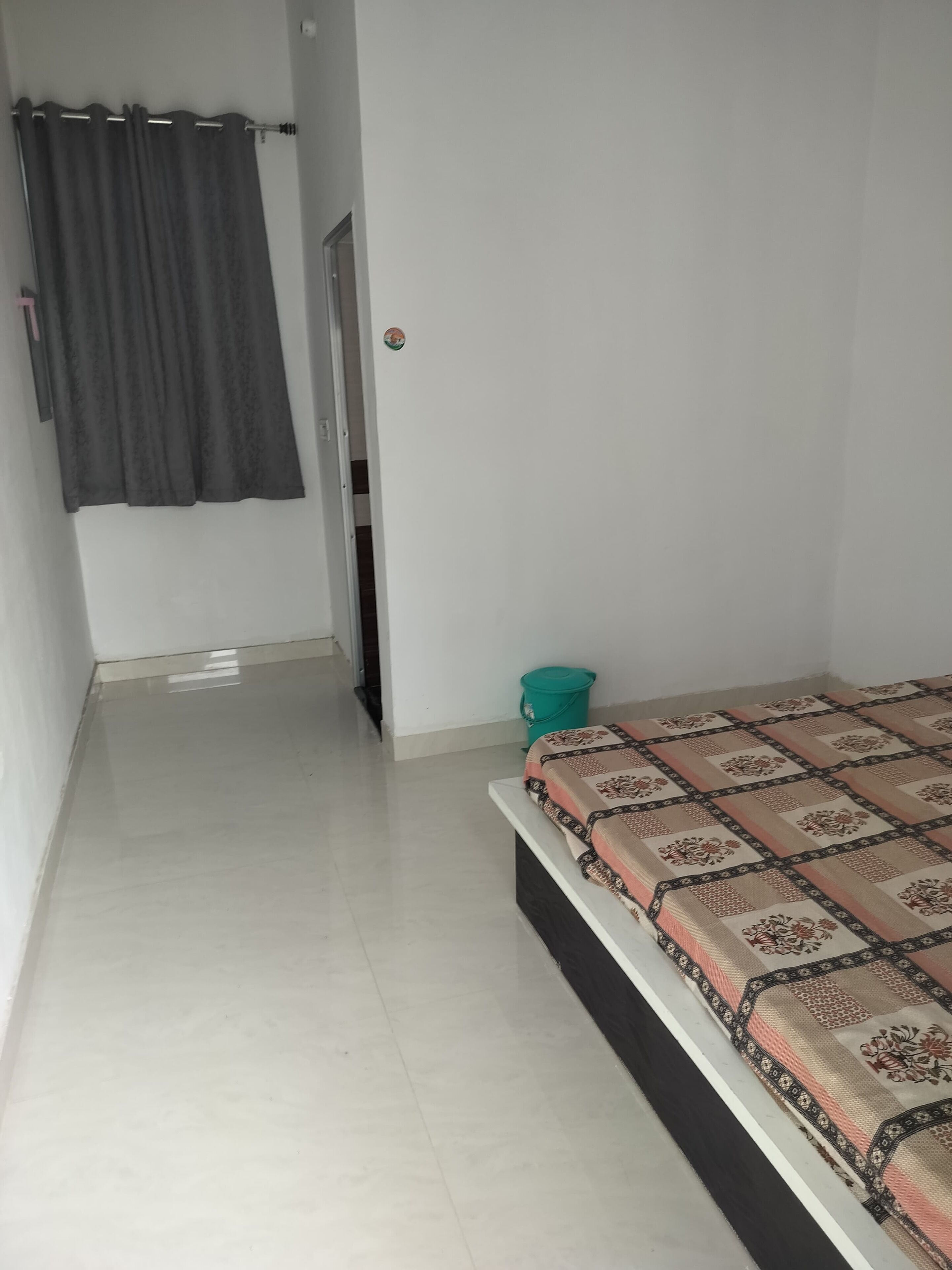 A bedroom with a bed, a curtain, a bucket, and a door.