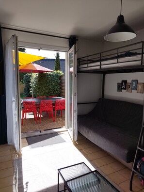 Et værelse med køjeseng, et bord med røde stole og en patio med en gul parasol.