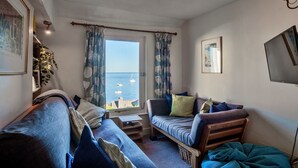 A cozy room with a sofa, a chair, and a small table. A window offers a view of the sea. - Penlee Narrows, Kingsand (Kingsand)