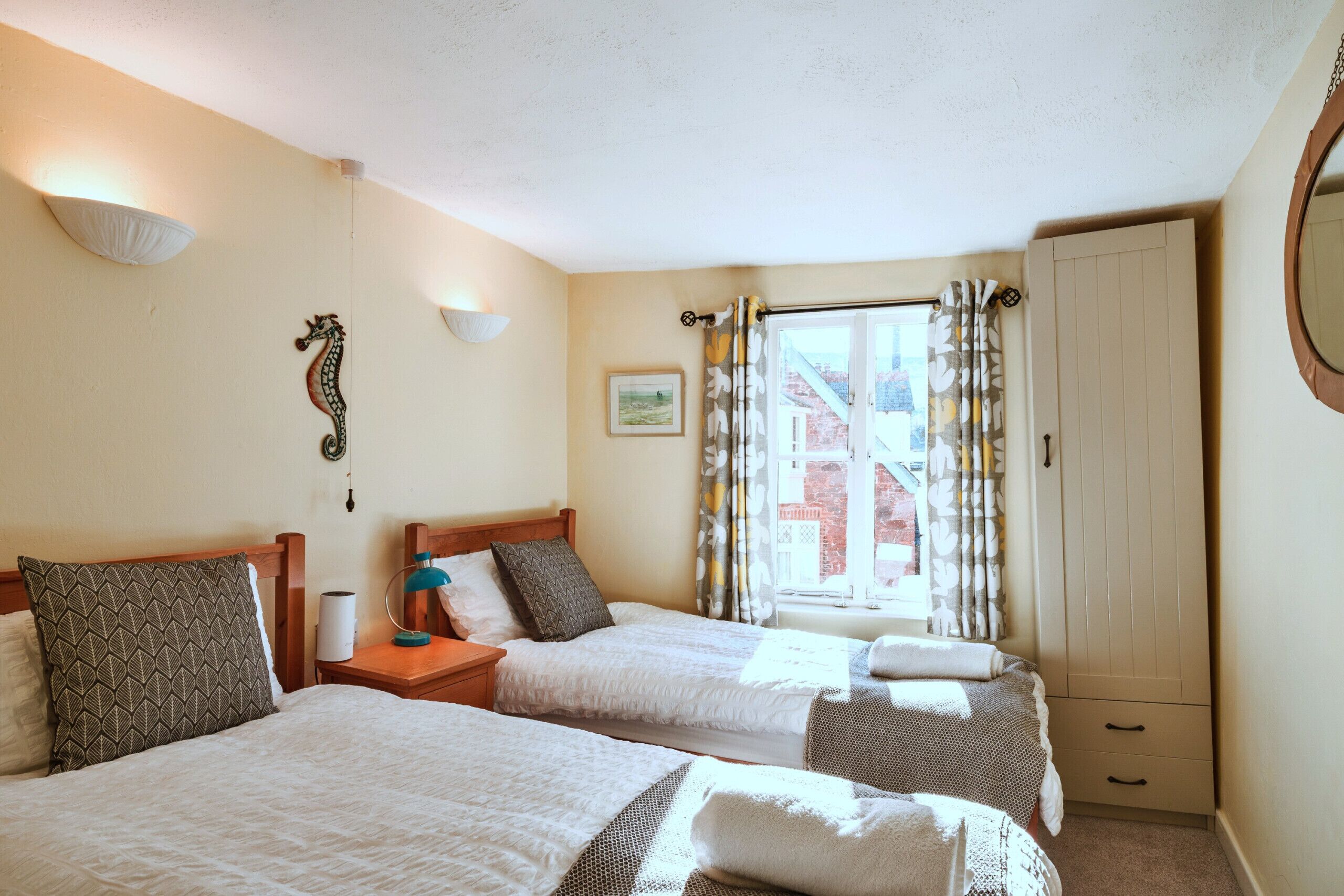 Een kamer met twee bedden, een garderobe, een raam met gordijnen en een wandlamp.