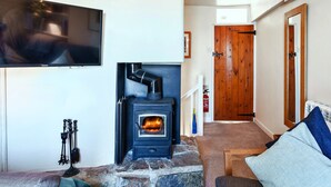 A living room with a stone fireplace, a mounted television, and a wooden door in the background. - Penlee Narrows, Kingsand (Kingsand)