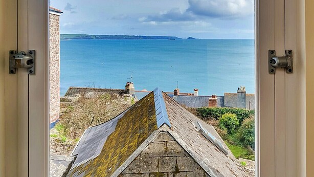 A view through a door of a coastal area with a clear sky, a body of water, and a stone structure with a sloped roof. - Penlee Narrows, Kingsand (Kingsand)