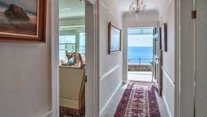 A hallway with a view of the sea, framed artwork, and a chandelier. - Penley Villa (Kingsand)