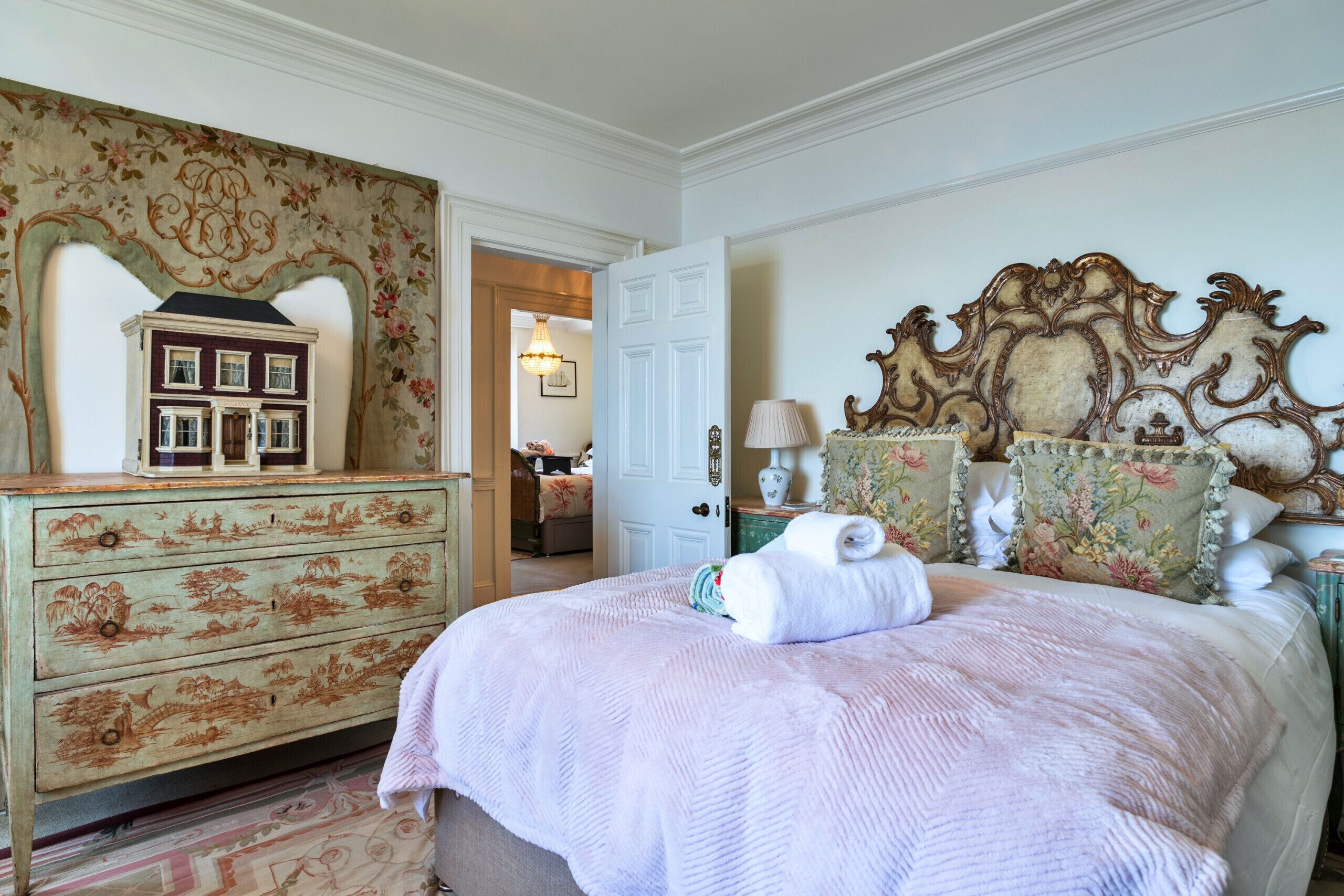 A bedroom with a bed, a dresser, and a door leading to another room.