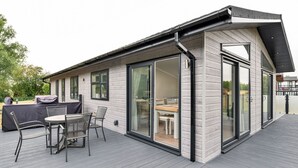 Une maison moderne dotée d’une terrasse, de grandes portes-fenêtres coulissantes et d’un coin repas aménagé avec du mobilier d’extérieur.