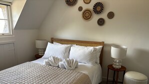 Una cama bien tendida con un edredón texturizado, dos lámparas de noche y una pared decorada con elementos tejidos.