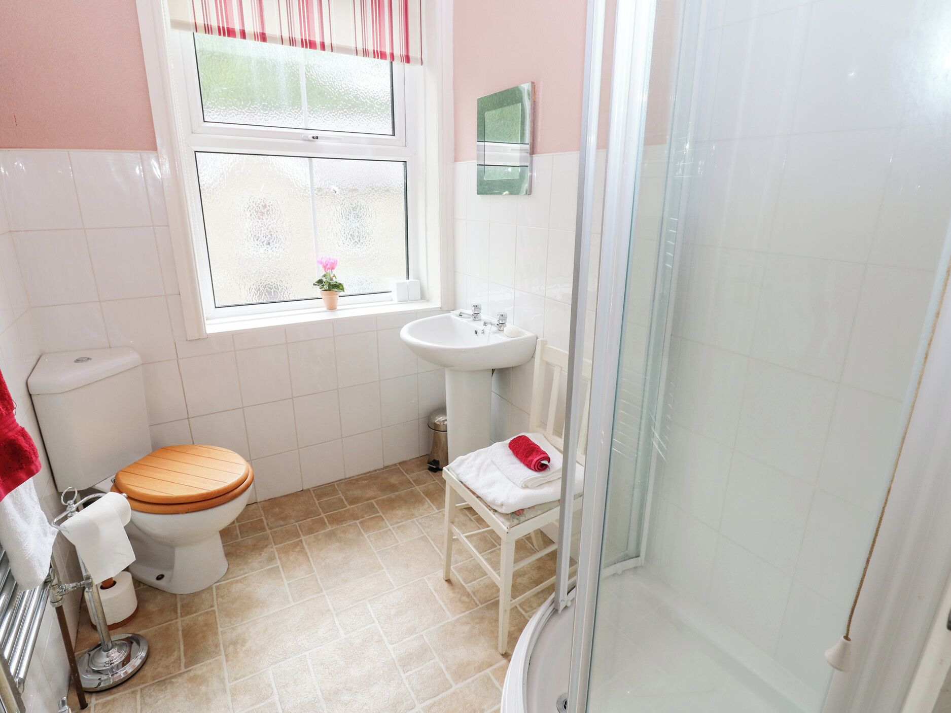 A bathroom with a toilet, sink, shower, and a window with a plant.