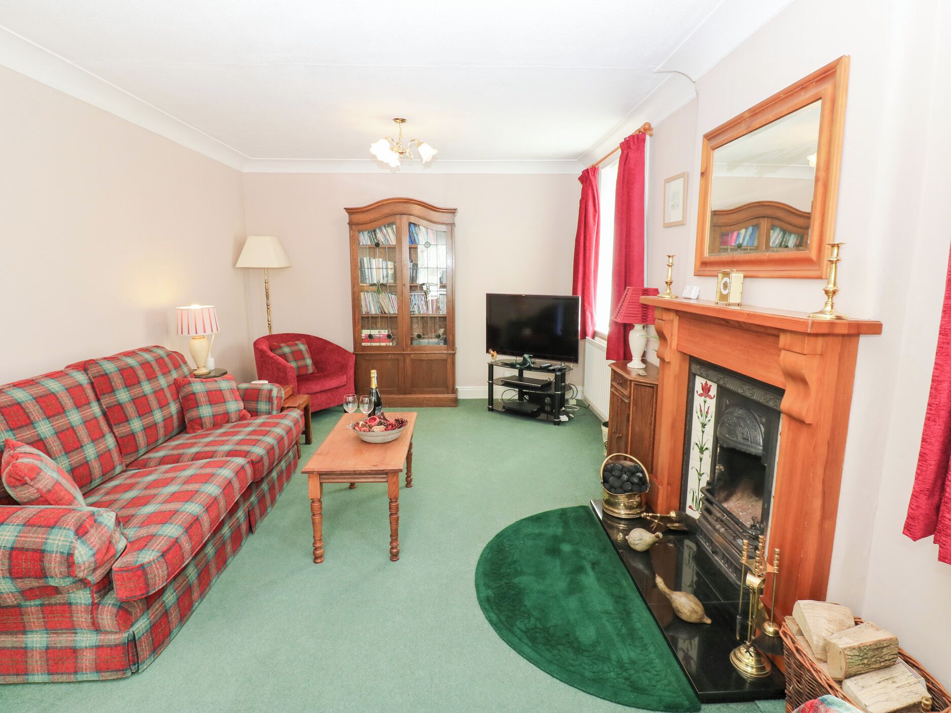 A living room with a red plaid sofa, a wooden cabinet with glass doors, a television, and a fireplace.