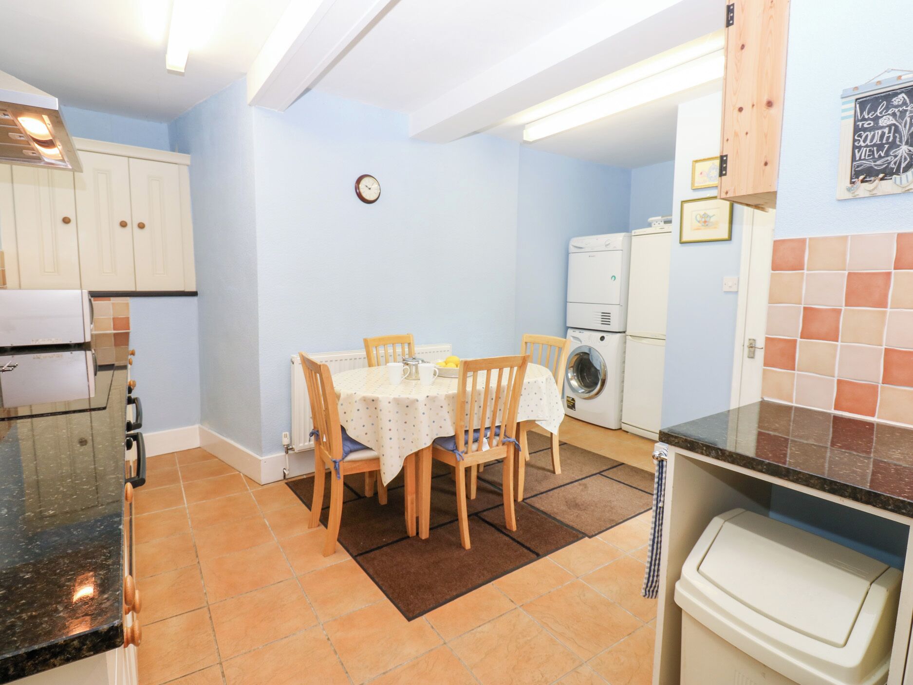 A compact kitchen with a dining table, chairs, and a clock on the wall.