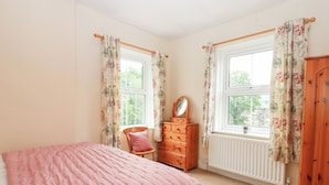 Un dormitorio con cama, cómoda, silla y ventanas.