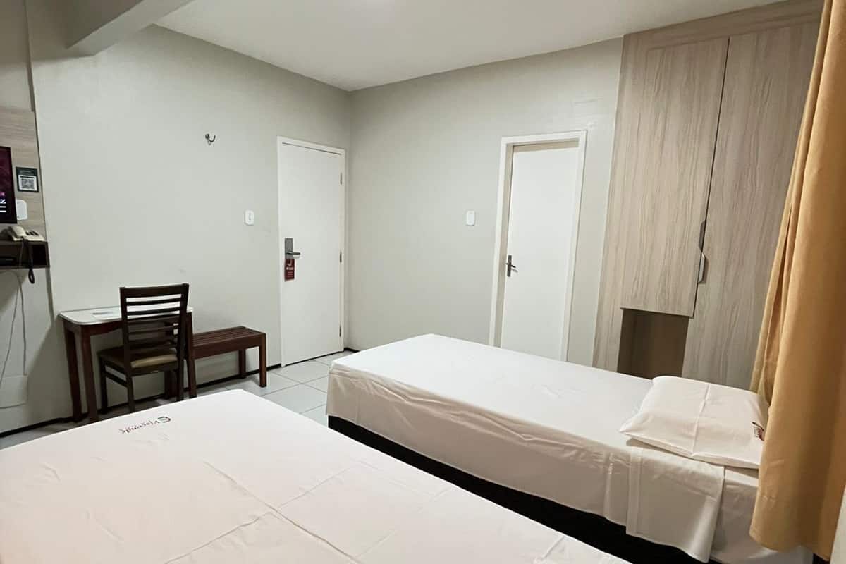A hotel room with two single beds, a desk, and a chair.