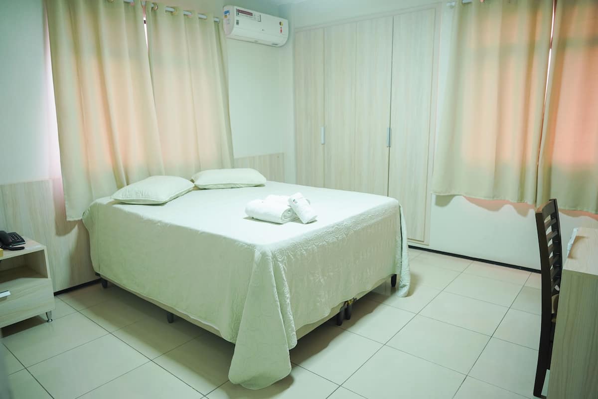 A neatly made bed with pillows and a rolled towel, a bedside table with a phone, and a chair.