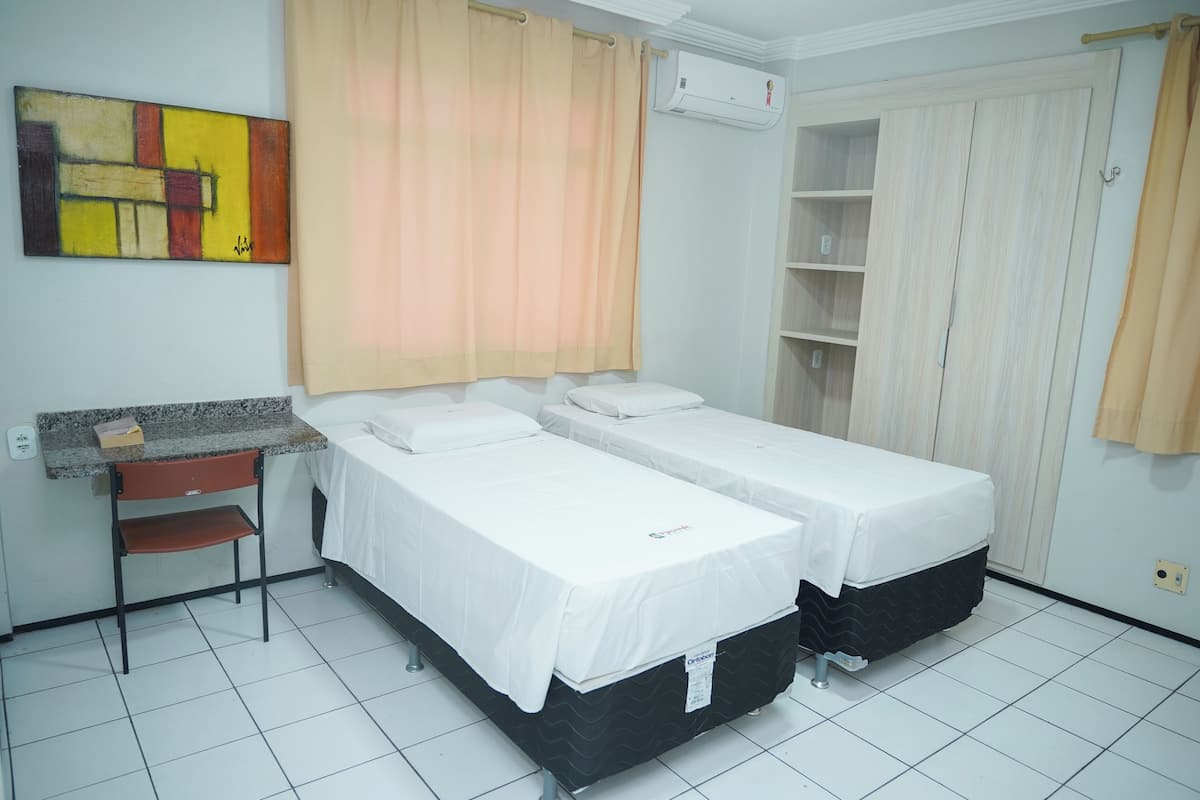 A room with two beds, a desk, a chair, a shelf unit, and a painting on the wall.