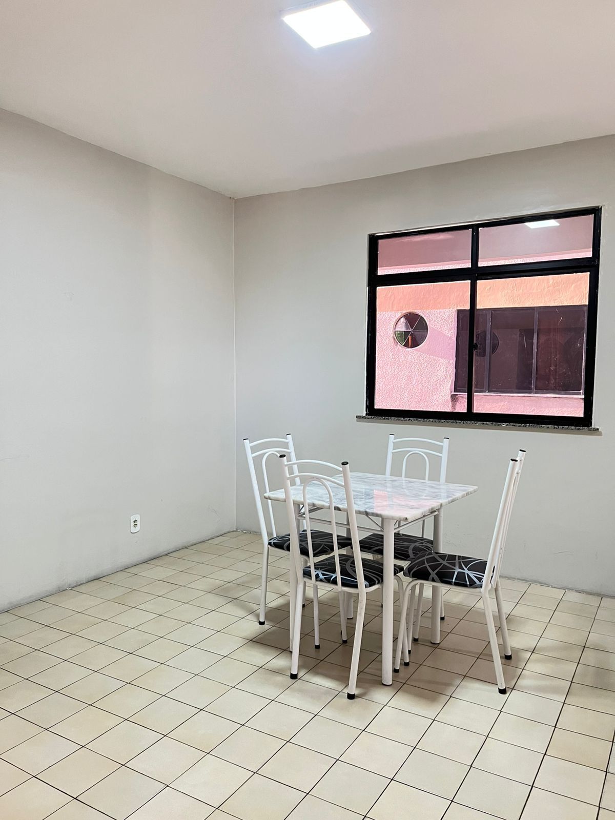 Una habitación con piso de baldosas, una mesa con cuatro sillas, una ventana con persianas y una lámpara en el techo.