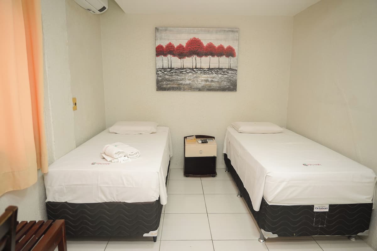 A room with two beds, a painting on the wall, and a suitcase on the floor.