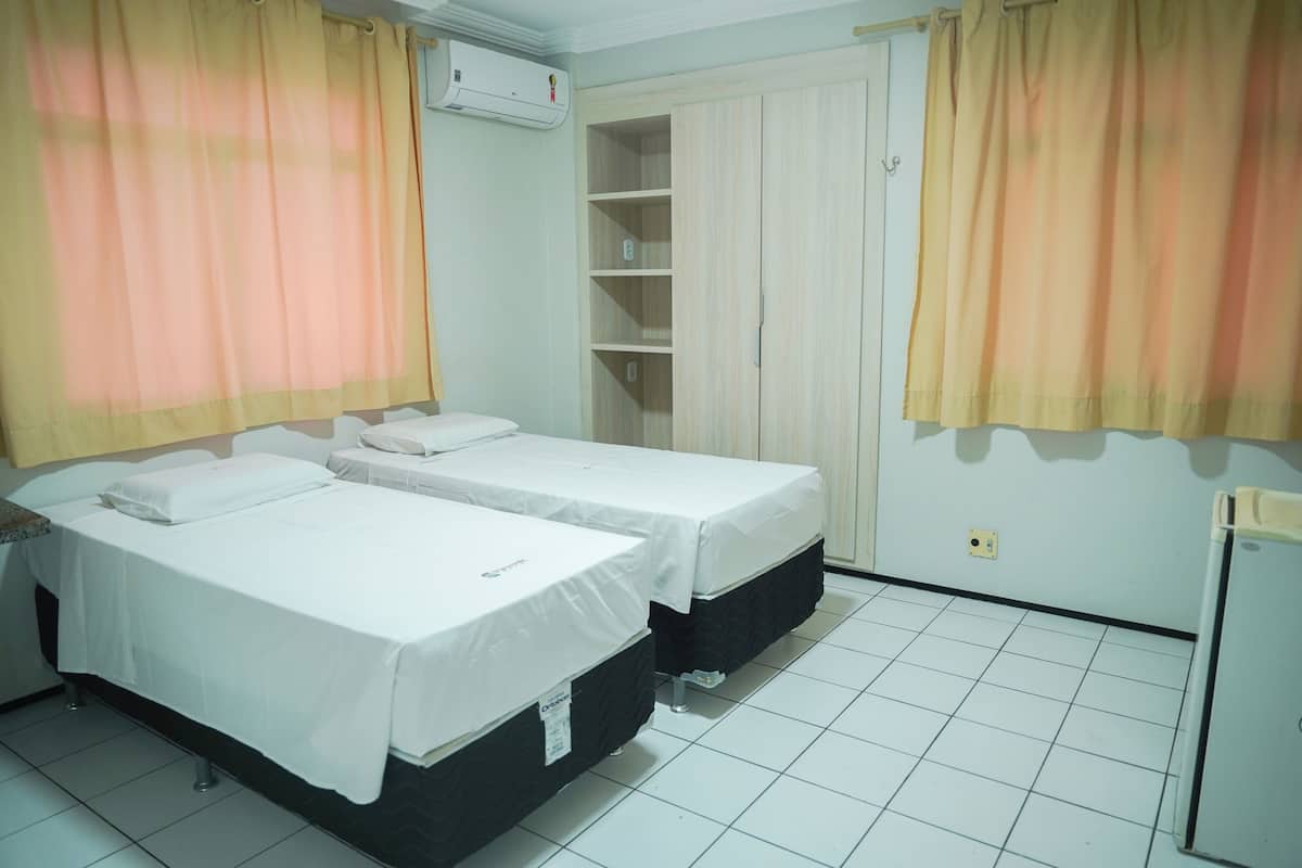 A room with two beds, a wardrobe, a shelf unit, and a small refrigerator.