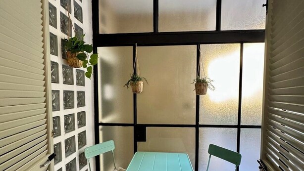 A small, enclosed room with a table and two chairs, a window with frosted glass, and a wall with a grid pattern. - Aro's House (Cremona)
