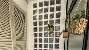 A small, enclosed patio area with a green metal table and chairs, a cushioned bench, and a wall with square windows. - Aro's House (Cremona)
