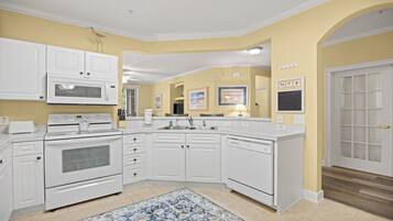A kitchen with white cabinetry, a microwave, stove, and dishwasher. There is a rug on the floor and a door with frosted glass panels.
