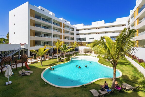 A modern hotel with a swimming pool, multiple balconies, and a well-maintained lawn. - 2BR Gardenia Retreat - Picuzzi & Pool (Punta Cana)