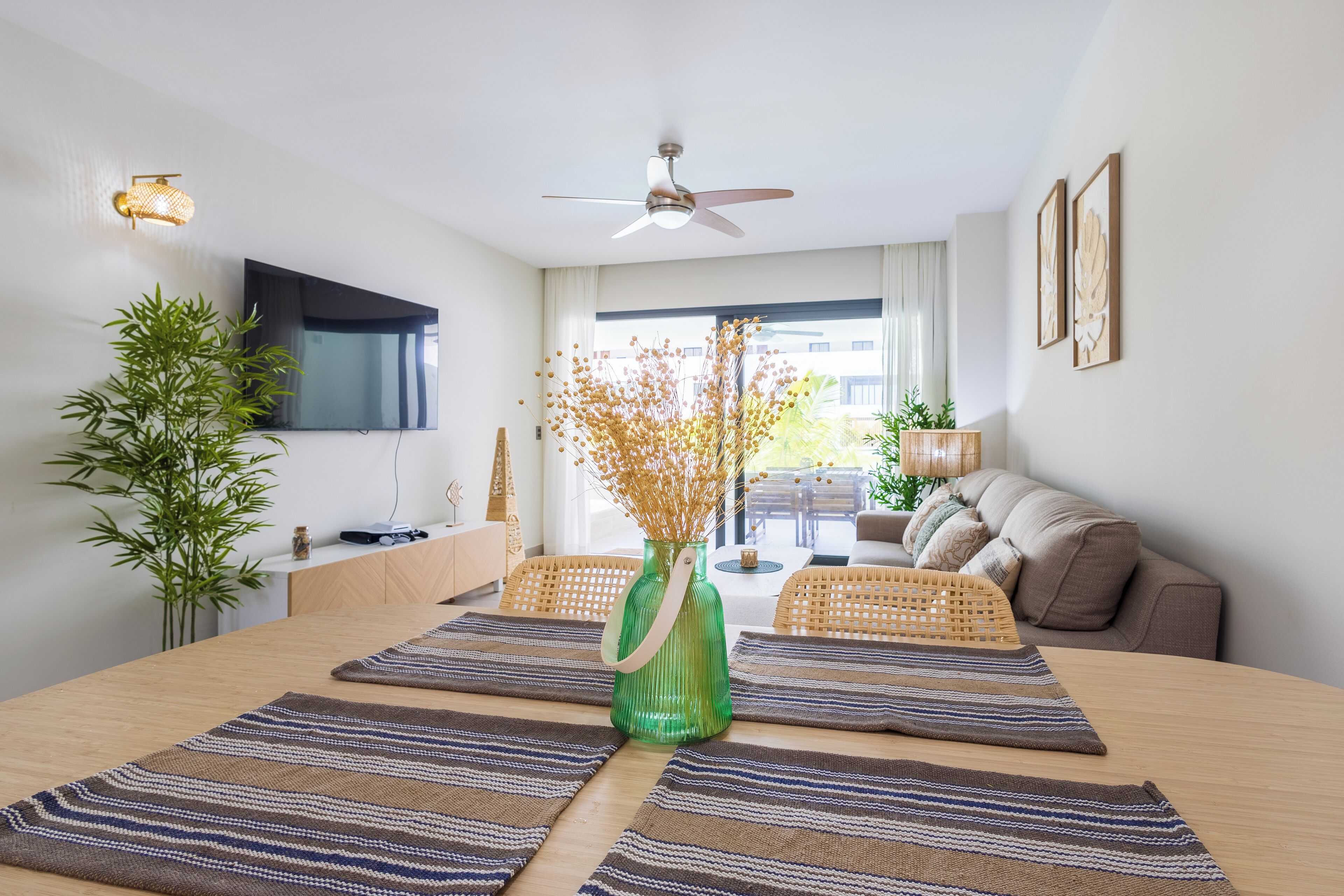Ein modernes Wohnzimmer mit Essbereich, inklusive Deckenventilator, Flachbildfernseher, einer grünen Vase mit Trockenblumen und einer Couch mit Kissen.