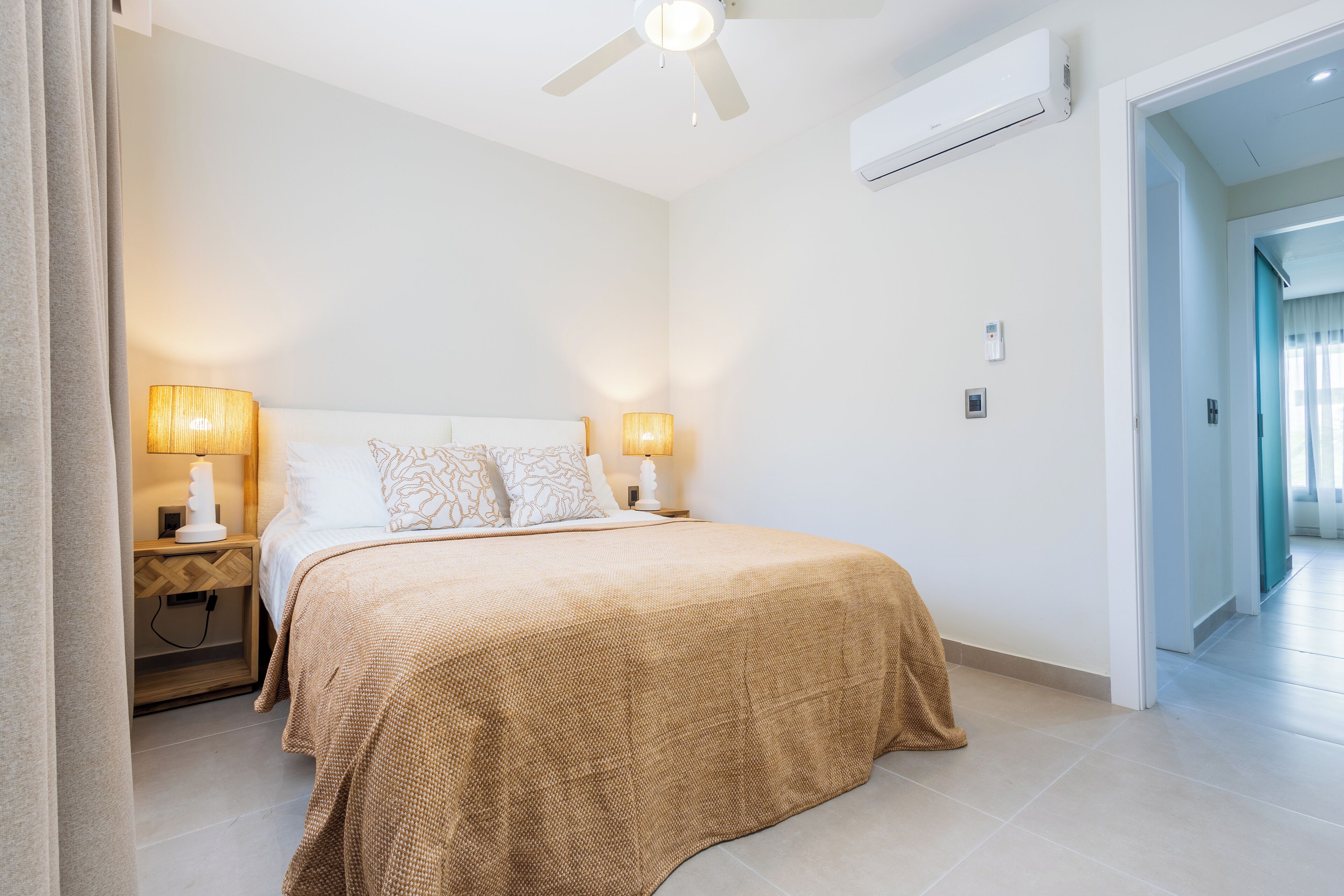A bedroom with a bed, two bedside lamps, a ceiling fan, and an air conditioning unit.