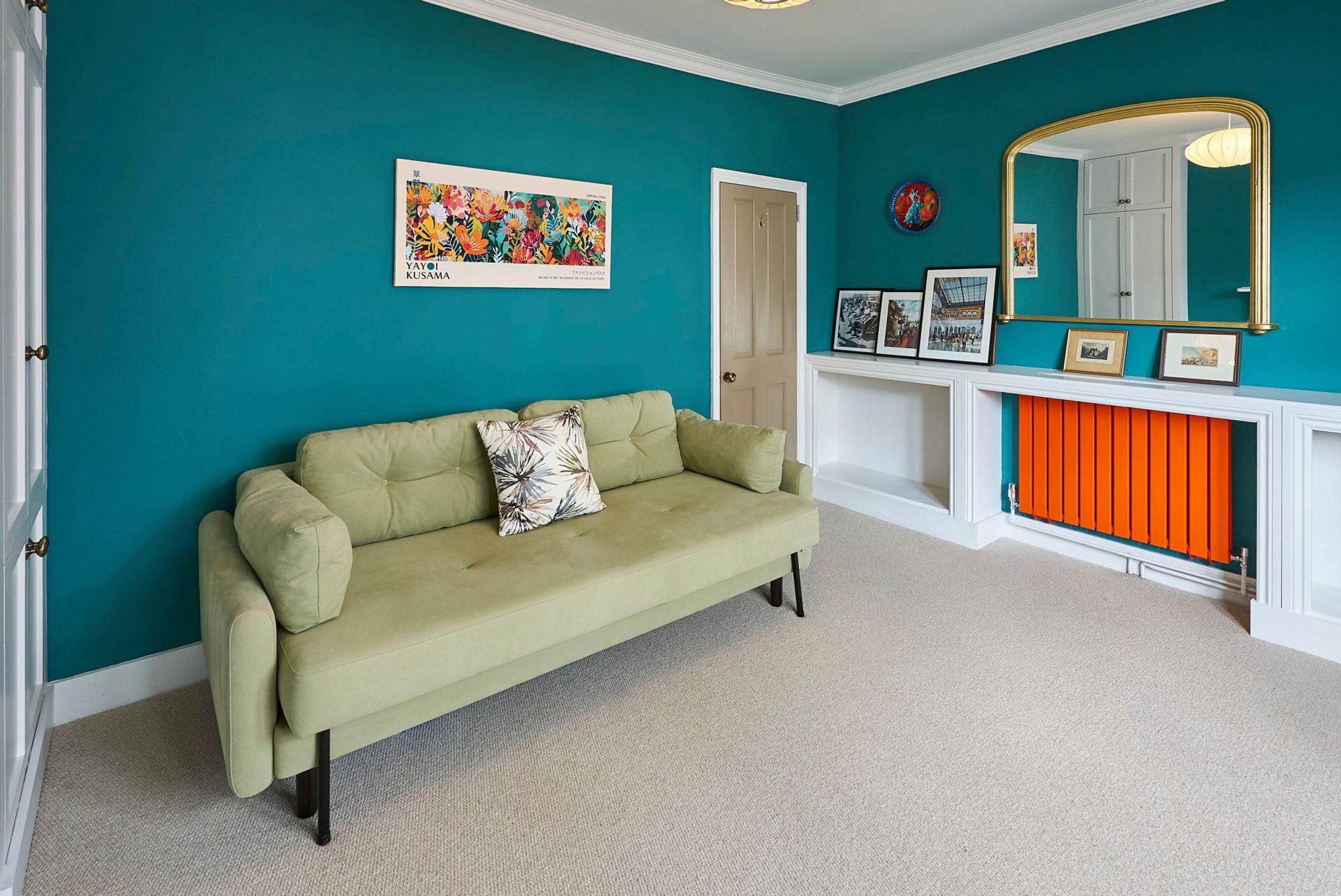Une pièce aux murs de couleur turquoise, avec un canapé vert, une cheminée ornée de motifs orange et un miroir à cadre doré.