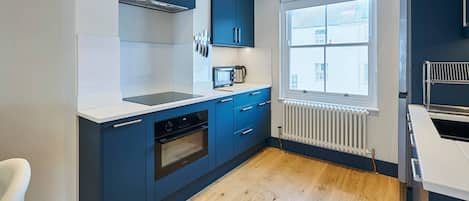 Een moderne keuken met blauwe kastjes, een wit aanrecht, een ingebouwde oven en een raam dat voor natuurlijk licht zorgt.
