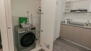 Ein Waschraum mit Waschmaschine, einem grünen Eimer und einem Wäschekorb.