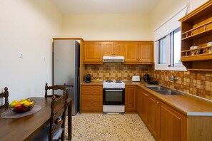 A compact kitchen with wooden cabinets, a stainless steel refrigerator, a built-in oven, and a tiled backsplash. - Valira Stathmos Home - Rustic Charm Cottage W Garden (Messini)