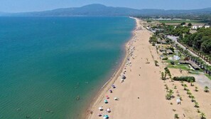 An aerial view of a beach with a long stretch of sand, a few umbrellas, and a line of trees. - Valira Stathmos Home - Rustic Charm Cottage W Garden (Messini)