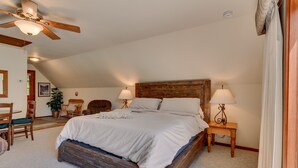 A bedroom with a wooden bed, two bedside tables with lamps, a ceiling fan, and a view of the outdoors.