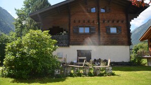 Un chalet en bois doté d’un balcon, entouré de verdure et de montagnes.