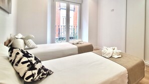 Een hotelkamer met twee bedden, een raam met uitzicht op een gebouw van rode bakstenen, een witte lamp en een witte badjas op het bed.