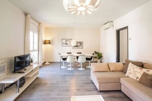 Un salon moderne comprenant un canapé, un téléviseur et un coin repas avec des chaises et une table.
