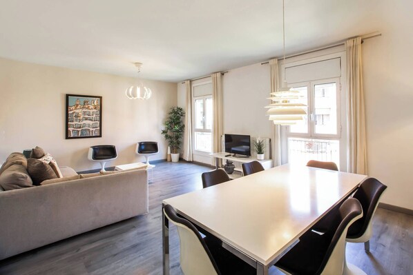 Un salon moderne avec un canapé, une table à manger et des chaises. On y trouve également un téléviseur et une plante.