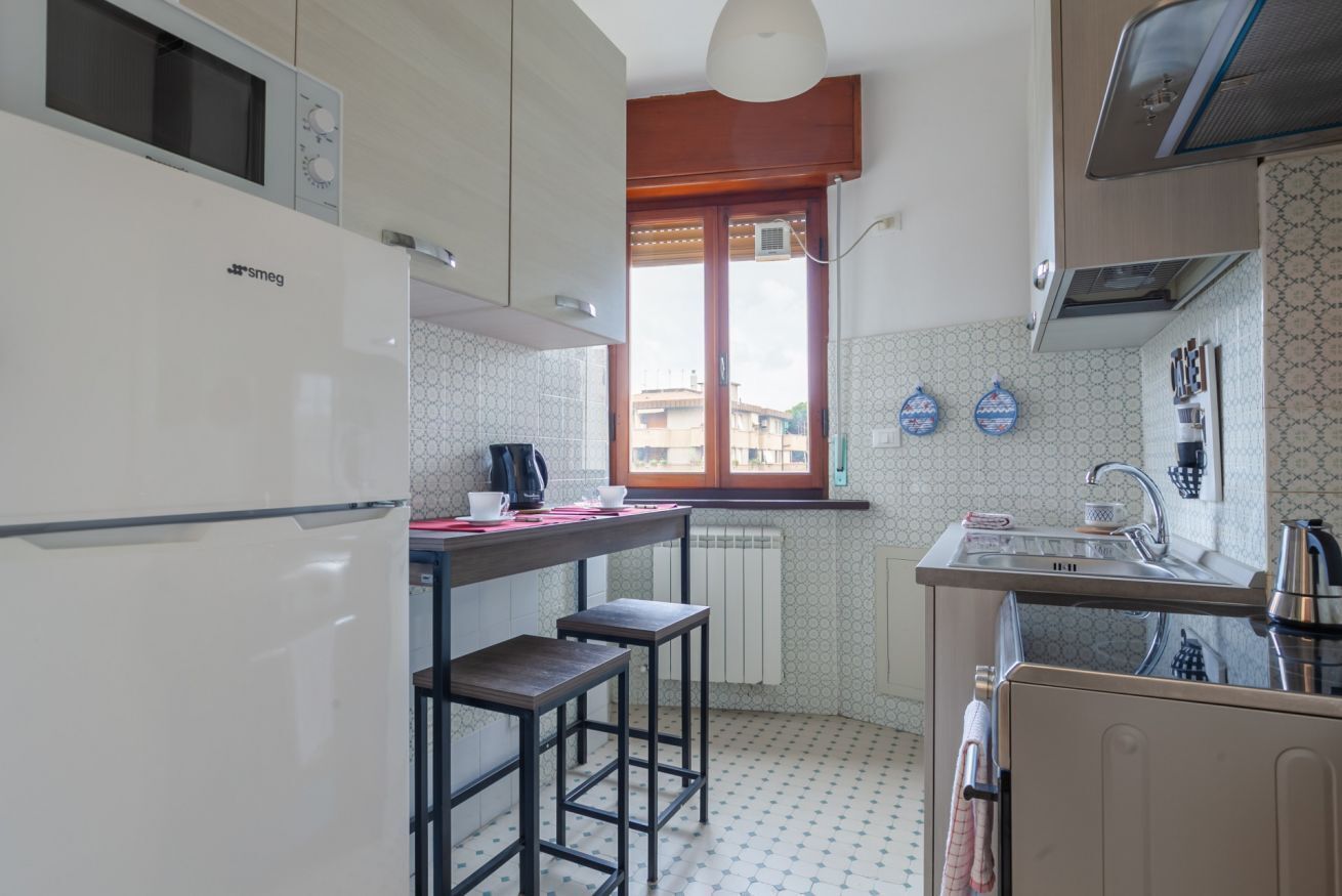Een kleine keuken met een koelkast, een raam, een spoelbak en twee krukken.