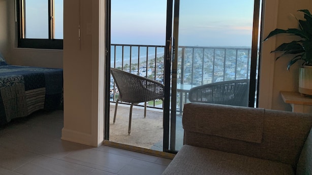 A balcony with a view of the beach and cityscape, a wicker chair, and a sofa. - Awesome II_Beach Views From the Bed (Myrtle Beach)