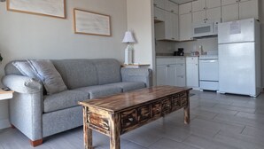 A living room with a grey sofa, a wooden coffee table, and a kitchen area with white cabinets and appliances. - Awesome II_Beach Views From the Bed (Myrtle Beach)