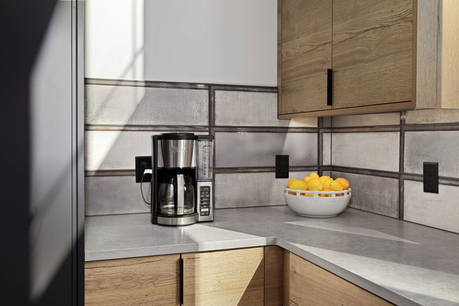 A kitchen with a coffee maker, a bowl of lemons, and wooden cabinets.