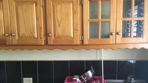 Eine Küche mit Holzausstattung, einer schwarzen Küchenzeile und einem rosa Geschirrgestell auf der Arbeitsfläche.