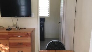 Ein kleines Zimmer mit einem Holztisch, einem an der Wand befestigten Fernseher und einer Tür, die in einen weiteren Raum führt.