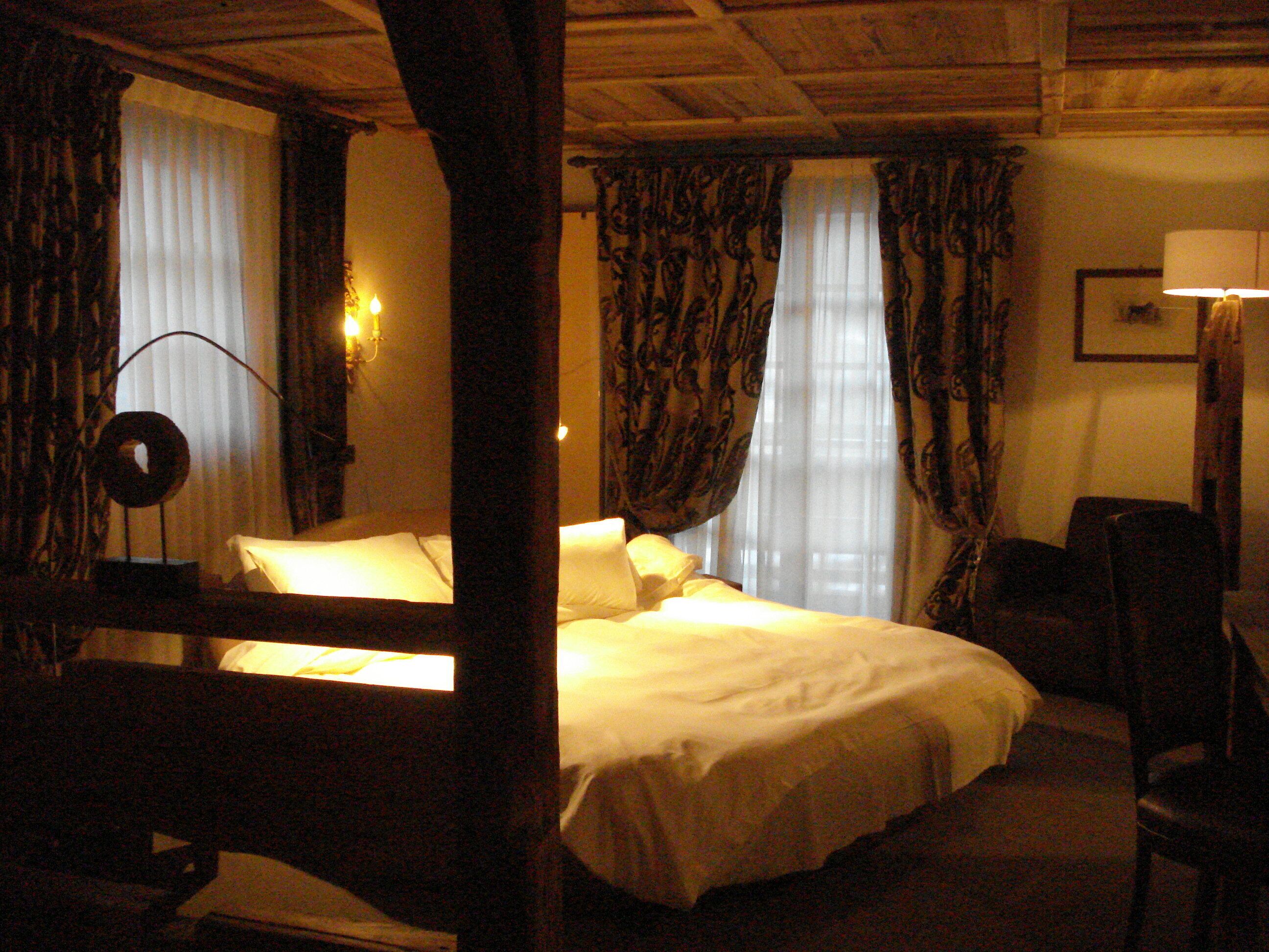 A room with a bed, a desk, and a chair. There are curtains on the windows.