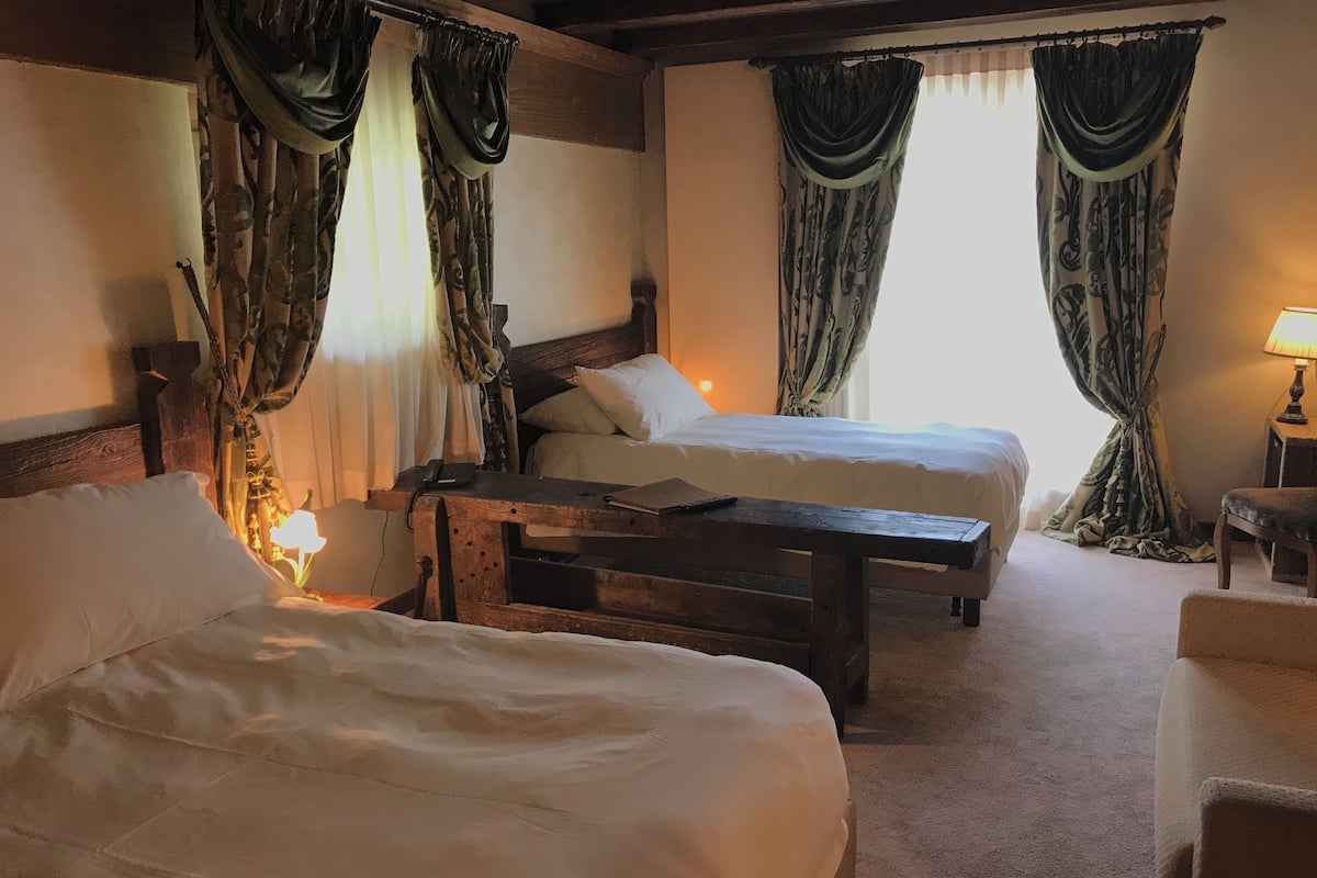 A hotel room with two beds, a wooden nightstand, a lamp, and curtains.