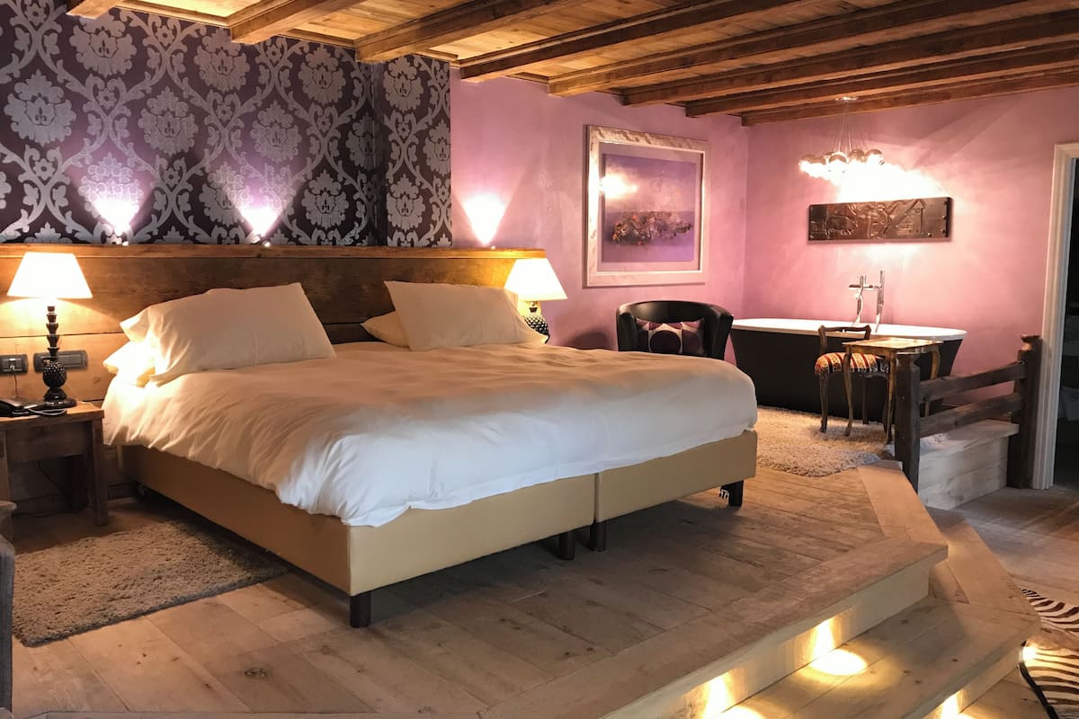 A bedroom with a large bed, wooden headboard, two bedside lamps, a desk with a chair, a zebra rug, and a framed picture on the wall.