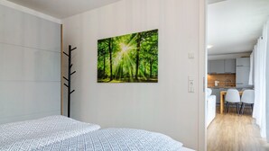 Una habitación de hotel moderna con una cama, un perchero, una zona de comedor con sillas y una cocina al fondo.