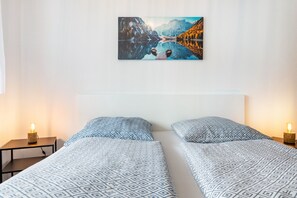 Een kamer met twee bedden, een schilderij aan de muur, bedlampjes en een wit hoofdeinde.